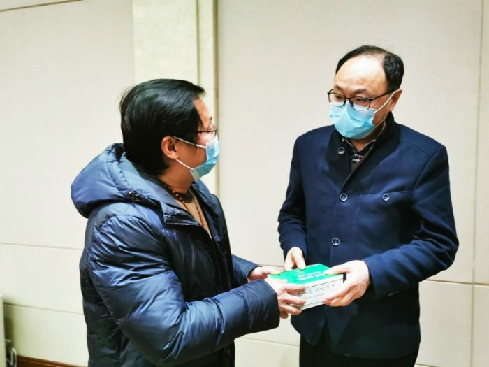 ▶王栋材（左）将4箱医用口罩送到了工作人员手中。
