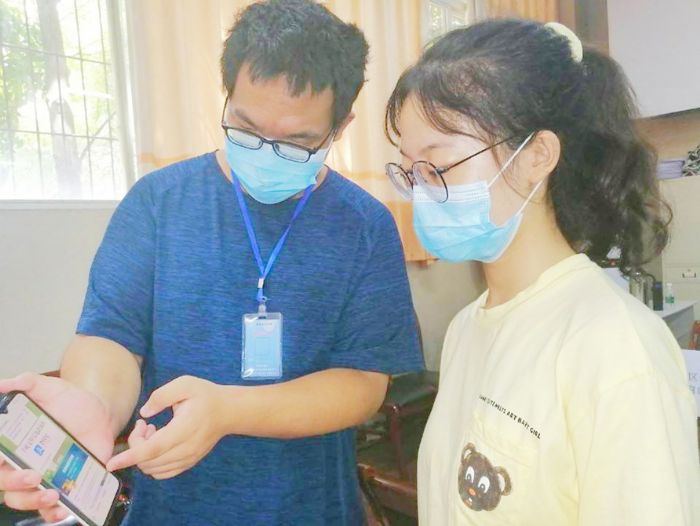 工作人员（左）指导学生利用手机注册贷款个人信息。
