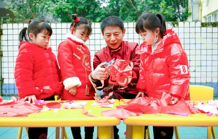 民间艺术家向孩子们传授剪纸技艺。
