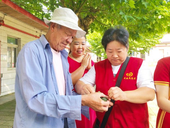 图②：志愿者和老人一起包粽子。

